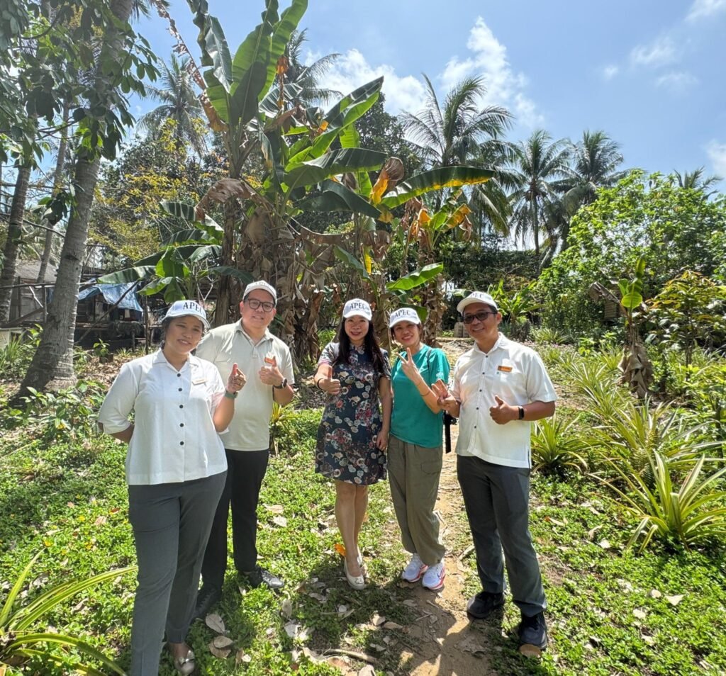 Five APEC participants posing together in a tropical garden